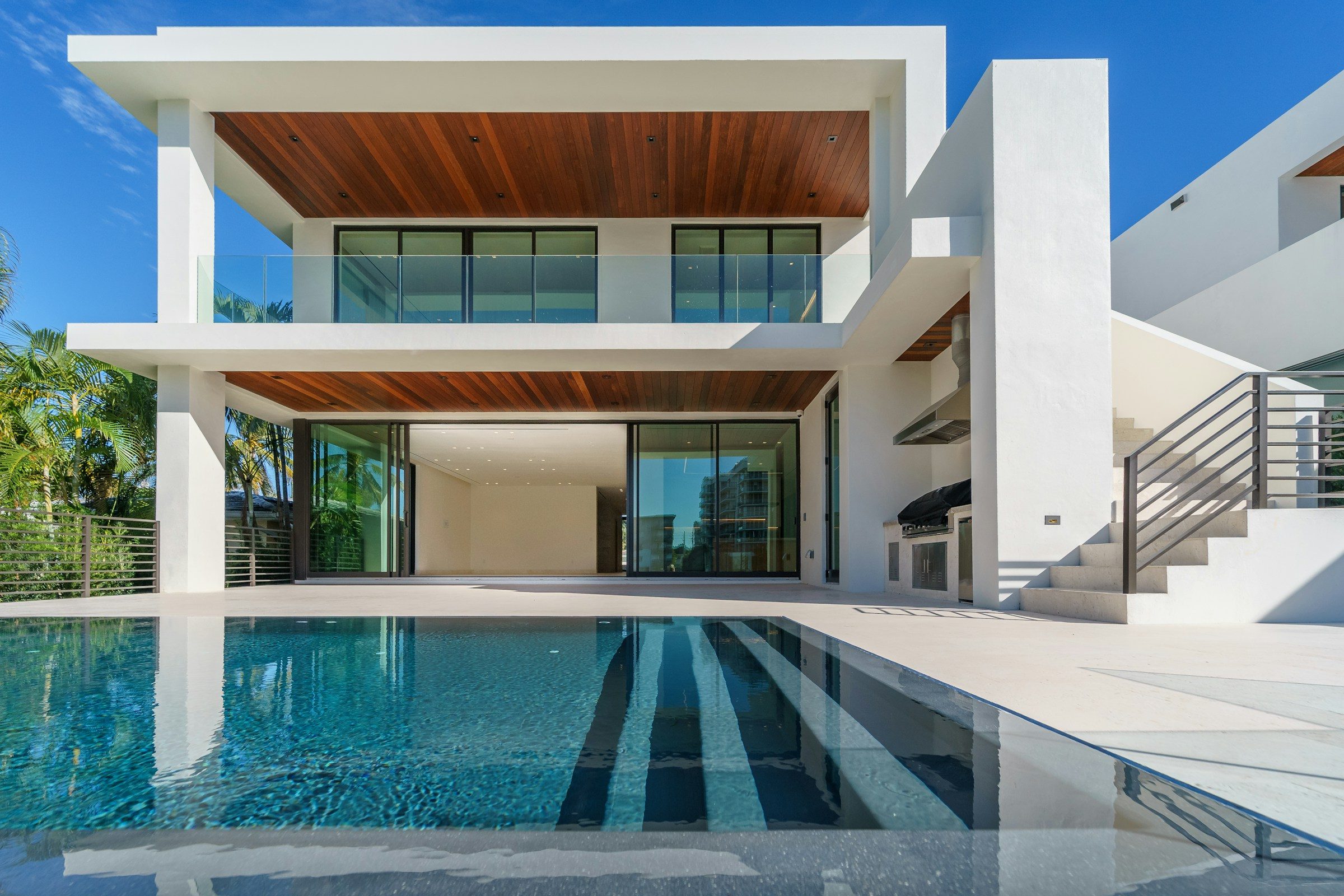 A modern white house with timber ceilings above an infinity pool